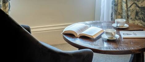 A room with a window, a table with a book and two cups, and a chair.