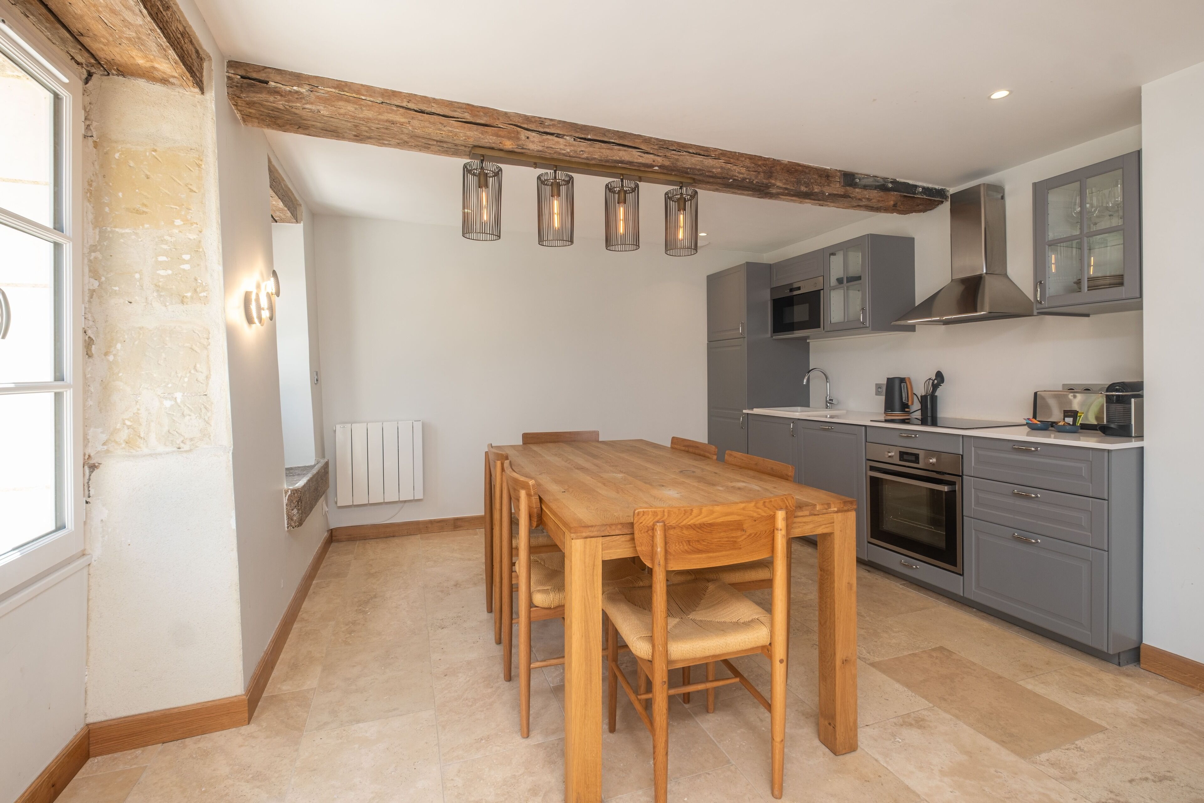 Une cuisine avec une table et des chaises en bois, des placards gris et un four encastré.