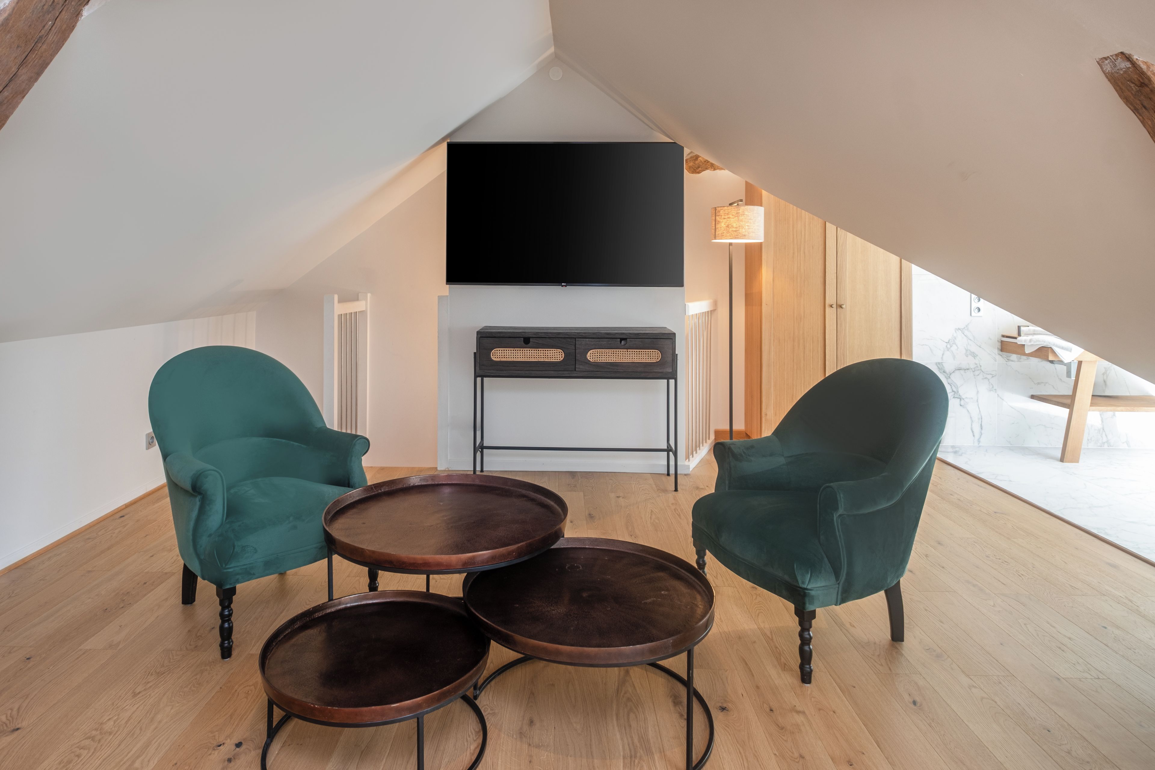 A modern loft bedroom with a large TV, two green chairs, and a small table.