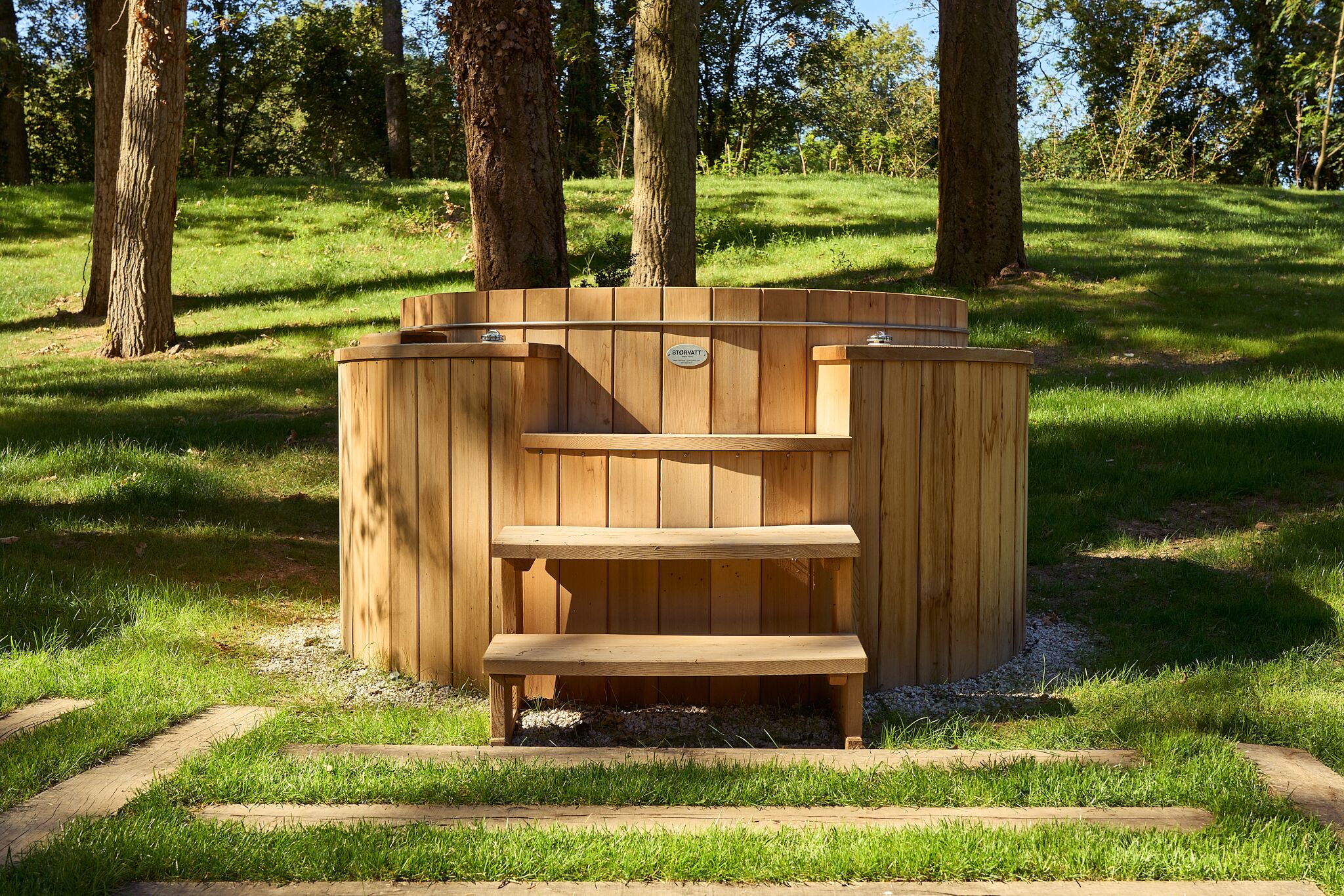 A wooden hot tub with a bench in a grassy park area.