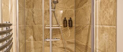 A shower with a glass door, marble tiles, and two bottles of shampoo.