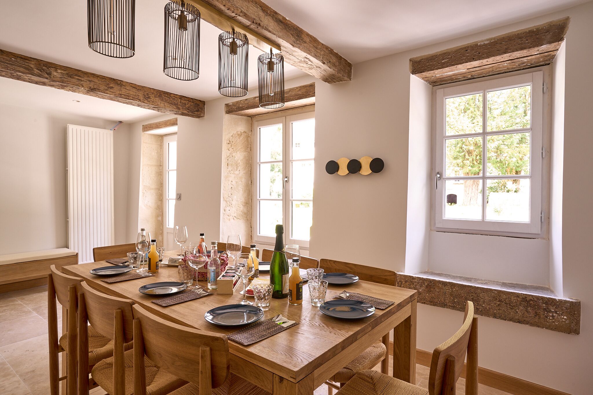 A dining area with a wooden table set for six, surrounded by chairs. There are hanging light fixtures above the table.