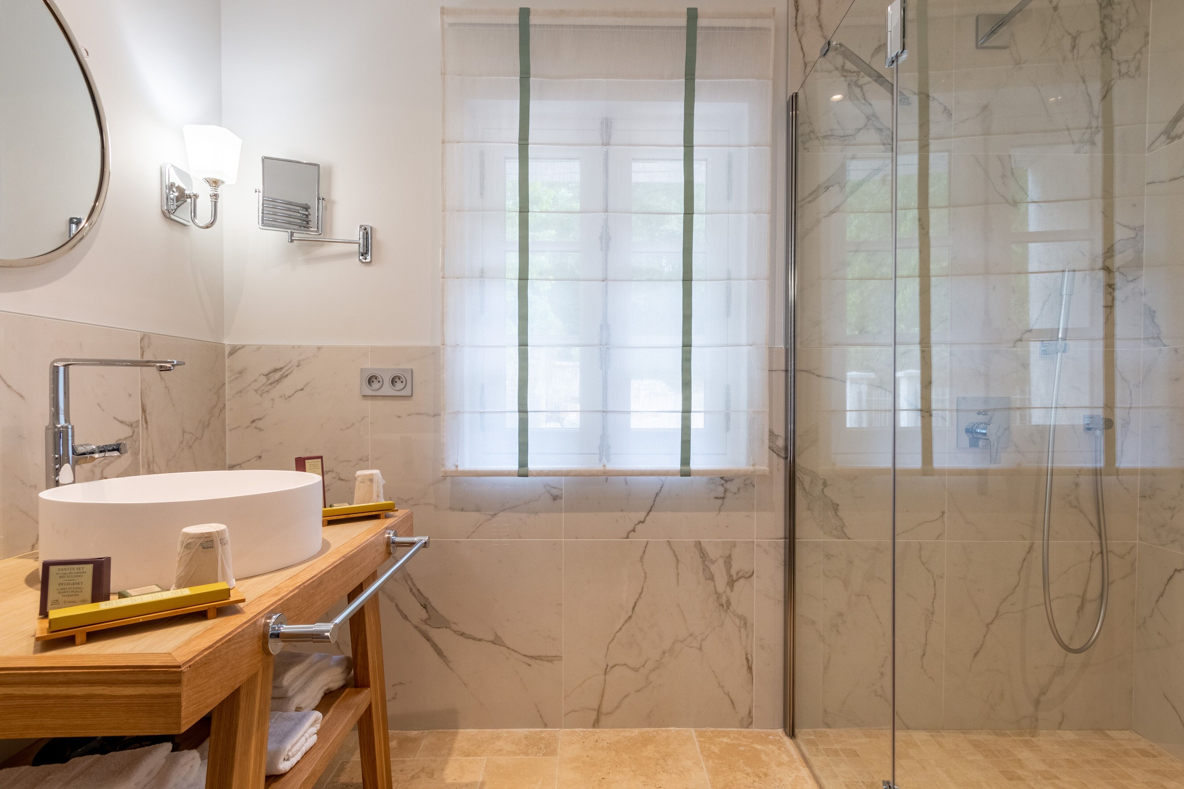 Un baño moderno con un lavamanos redondo, una cabina de ducha de vidrio y una ventana con persianas.