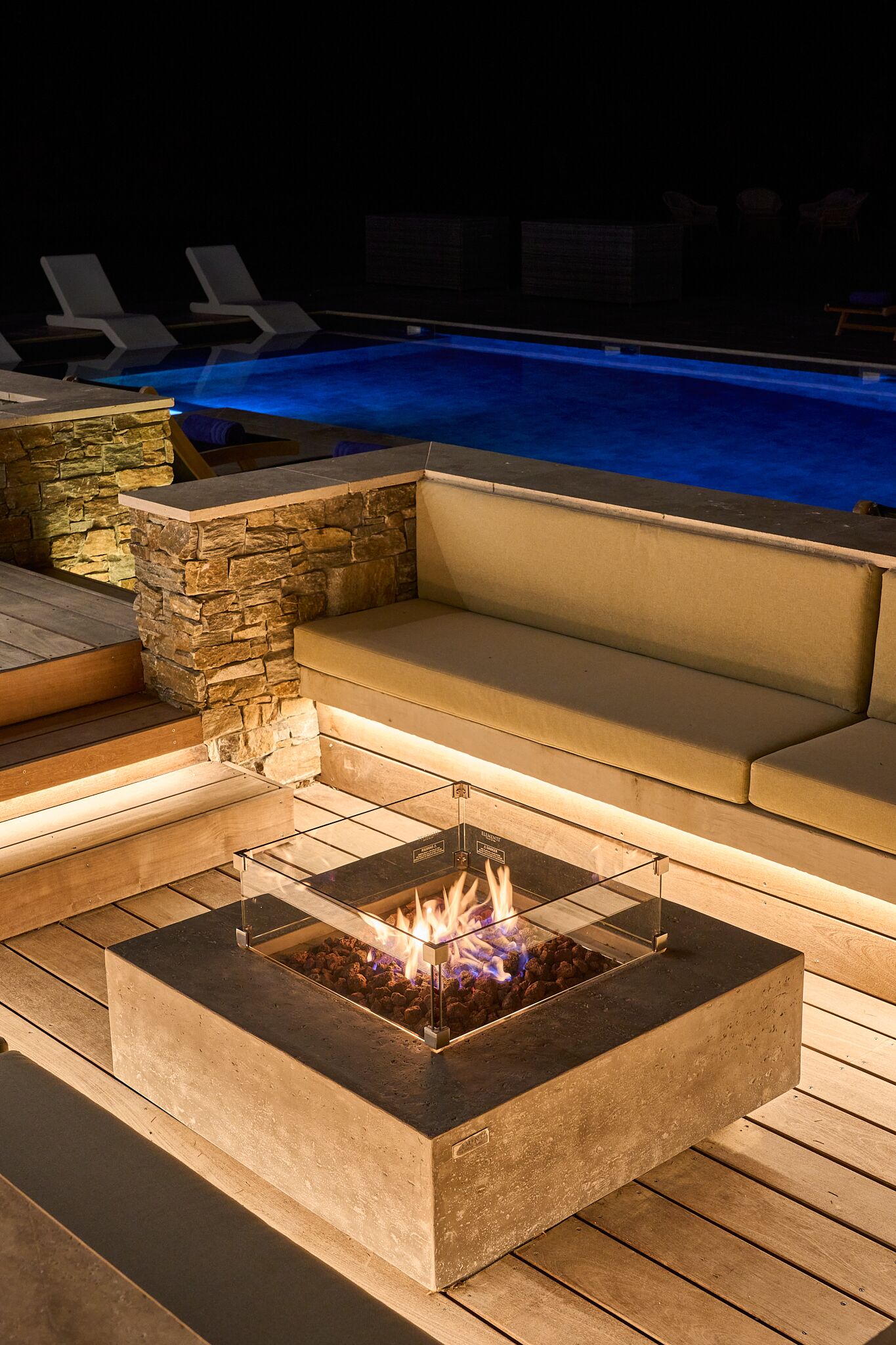 A poolside area with a fire pit, lounge chairs, and a stone wall.