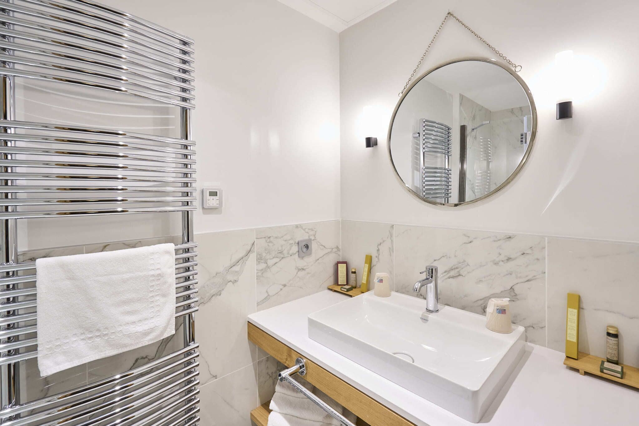 Une salle de bain moderne avec un lavabo blanc, un miroir rond et un porte-serviettes sur lequel est posée une serviette blanche.