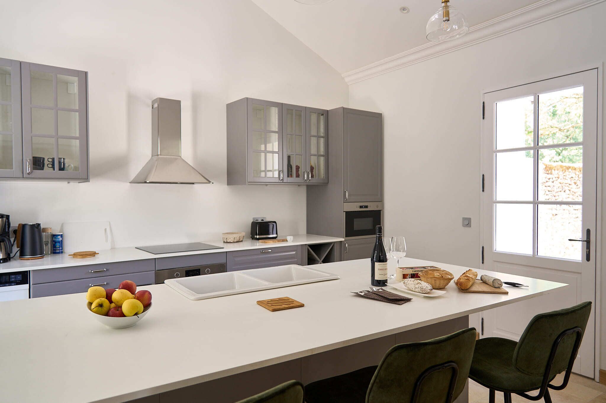 A modern kitchen with a large island, grey cabinets, and a view to the outside.