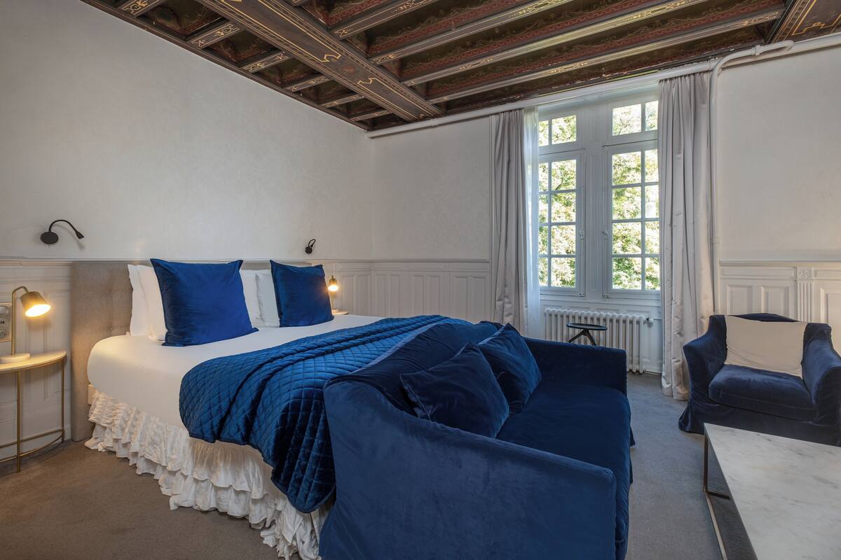 Ein Schlafzimmer mit einem großen Bett, einem Fenster mit Vorhängen, einem Schreibtisch und einem Stuhl.