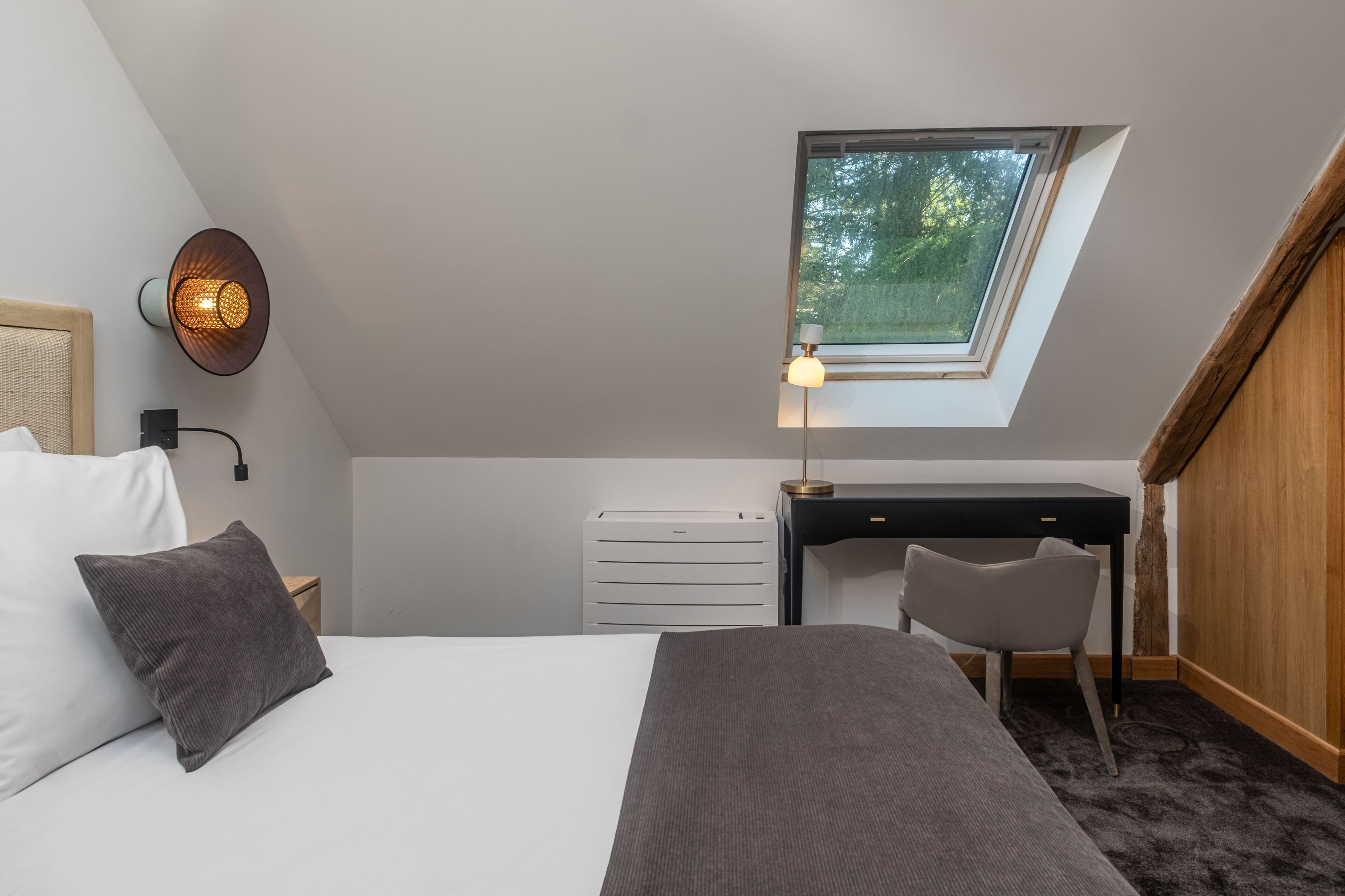 Une chambre avec un puits de lumière, un bureau, une chaise, un lit avec des oreillers et un radiateur.