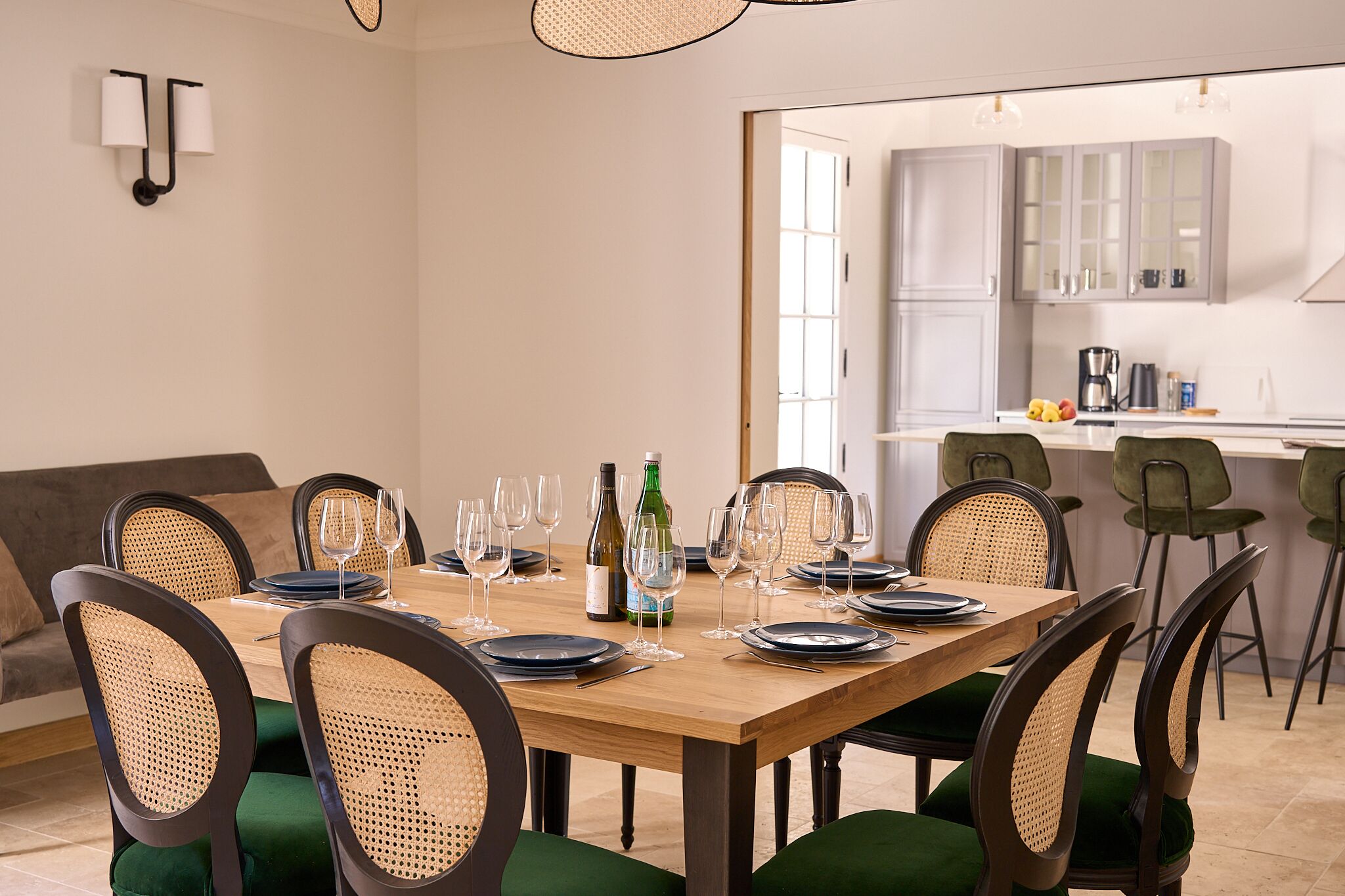 Comedor con una mesa de madera dispuesta para seis comensales, rodeada de sillas tapizadas de verde con respaldo trenzado.
