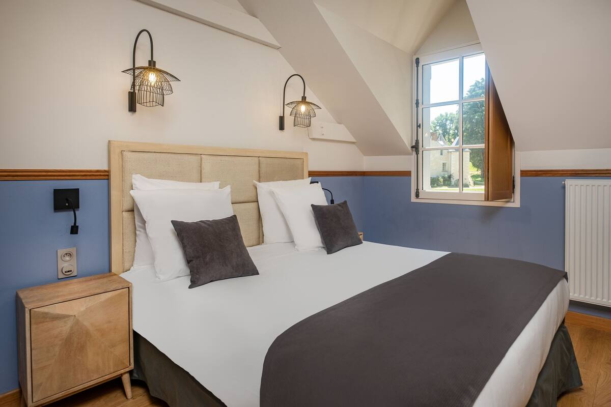 Ein Schlafzimmer mit einem großen Bett, zwei Wandlampen, einem Fenster mit Ausblick und einem Nachttisch aus Holz.