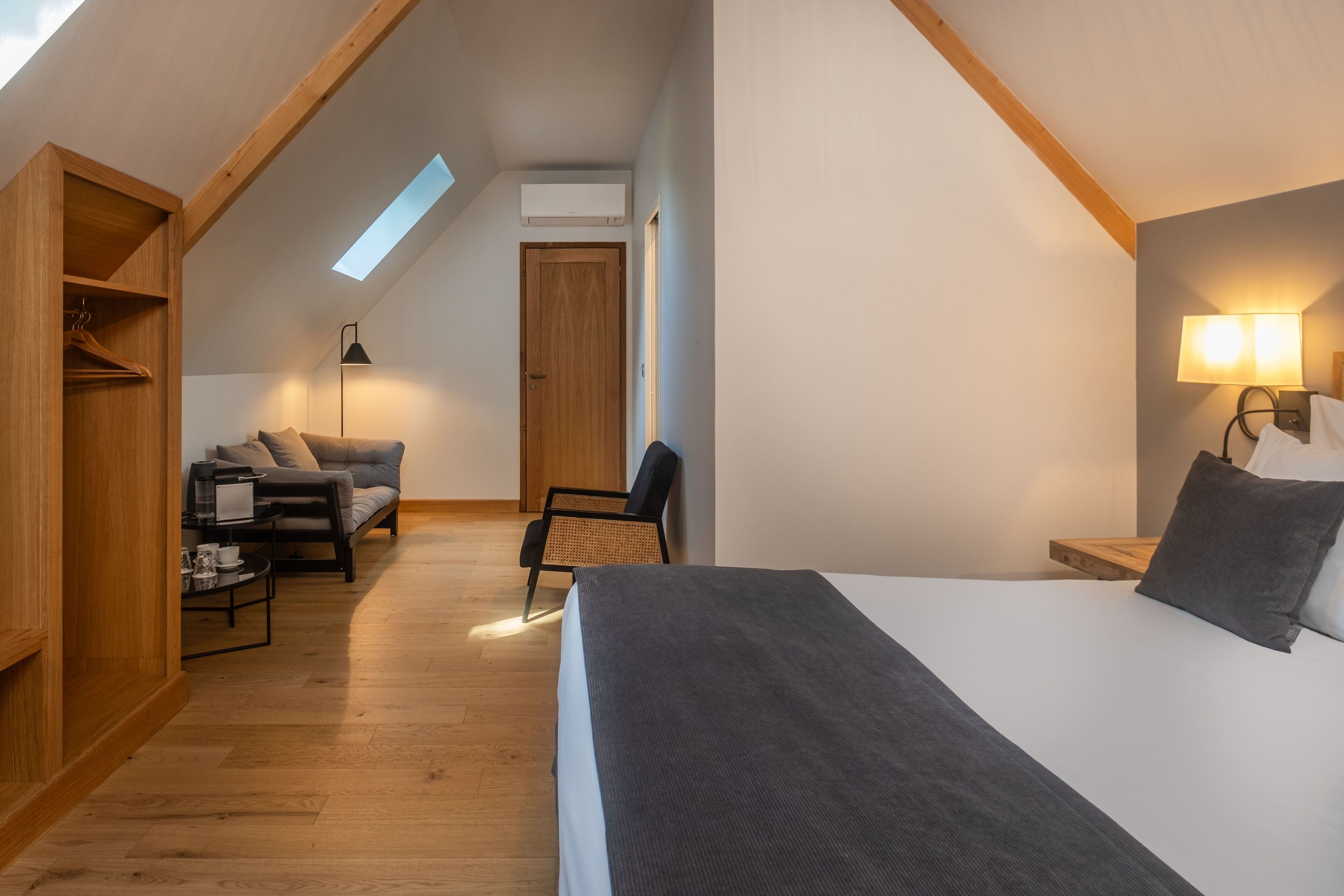Ein gemütliches Schlafzimmer im Dachgeschoss mit einem großen Bett, einem Schreibtisch und einem Stuhl. Es gibt ein Dachfenster, einen Holzschrank und eine Wandlampe.