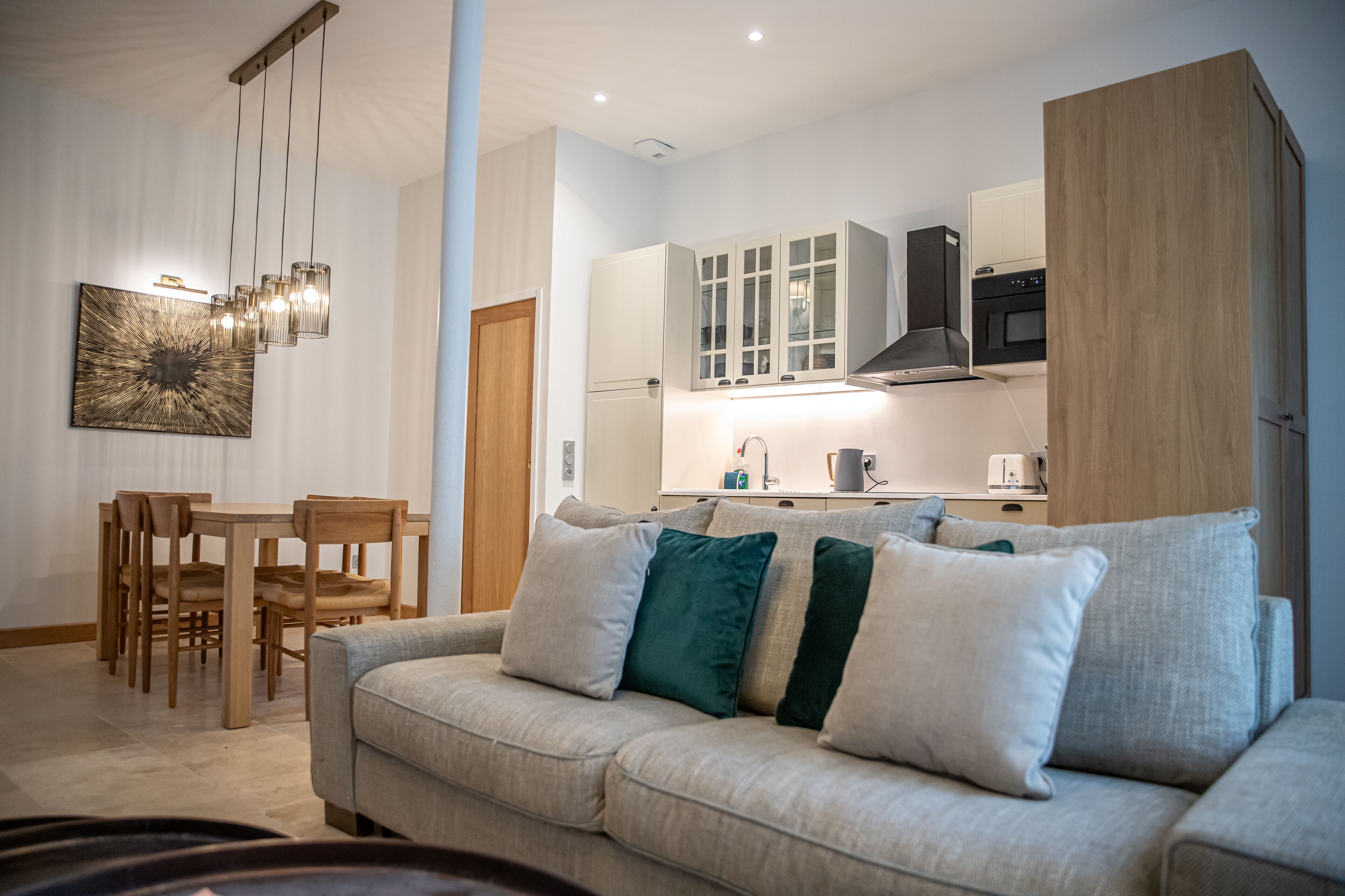 A modern living room with a sofa, a dining table with chairs, and a kitchen area with cabinets and a stove.