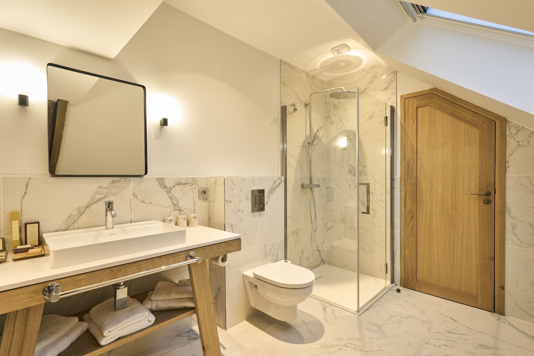 Une salle de bain moderne avec un lavabo en marbre, une douche à parois de verre et une porte en bois.