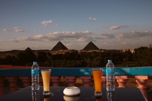 A table with two water bottles and two glasses of orange juice, with a view of pyramids in the background. - Heru Pyramids View Hotel (Giza)