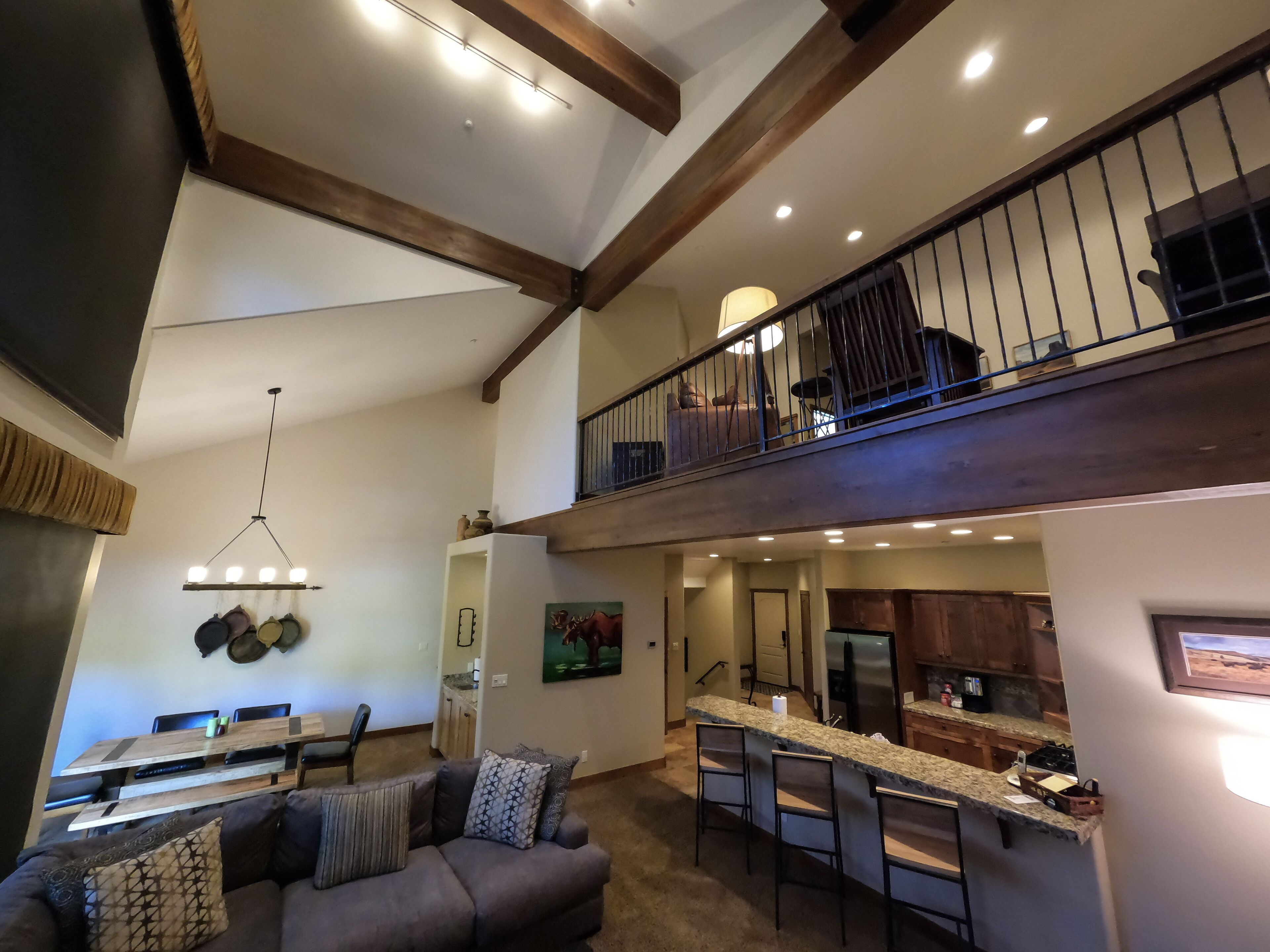 A spacious living area with a high ceiling, a dining table, a sofa, and a kitchen with a bar counter.