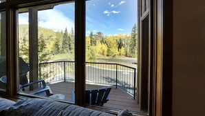 A room with a large window overlooking a deck with outdoor seating and a view of a forested mountain area. - Magnificent Townhome! Epic Mountain Views! Heated Pool! 2 Miles to Purgatory (durango)