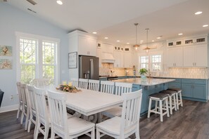 A spacious kitchen with white cabinetry, a large island, and a dining area with white chairs.