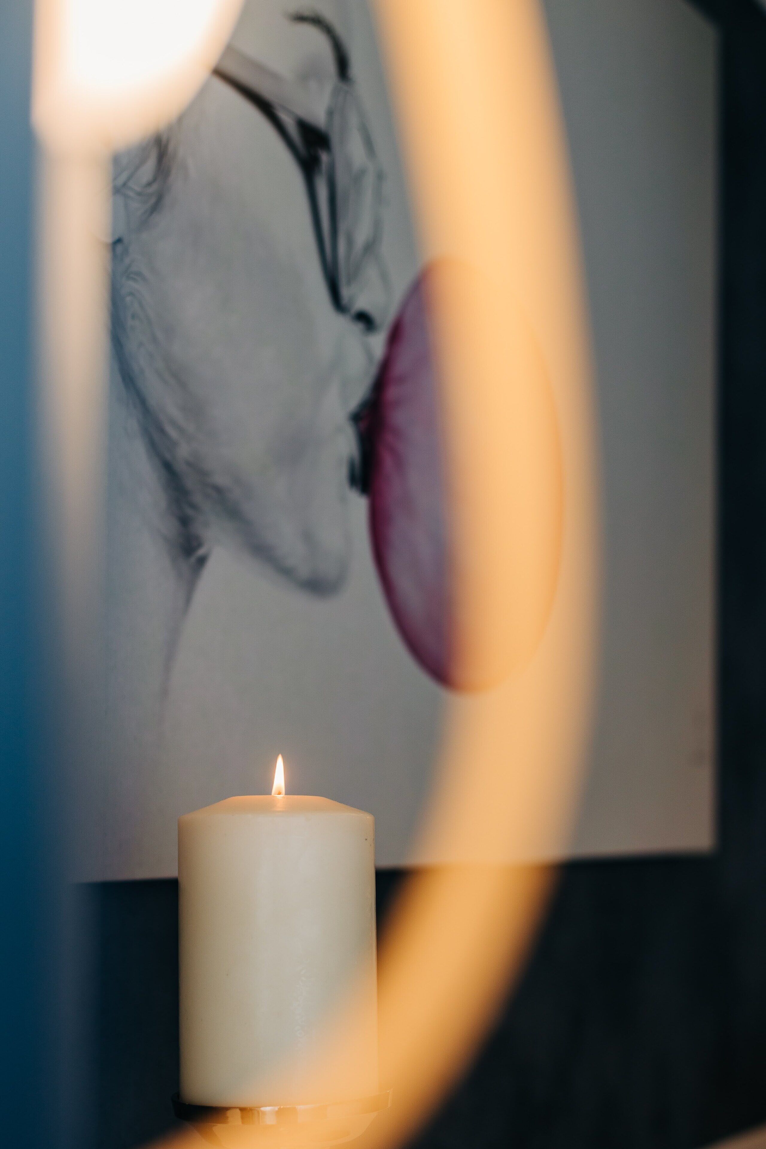 A candle on a table with a wall art in the background.