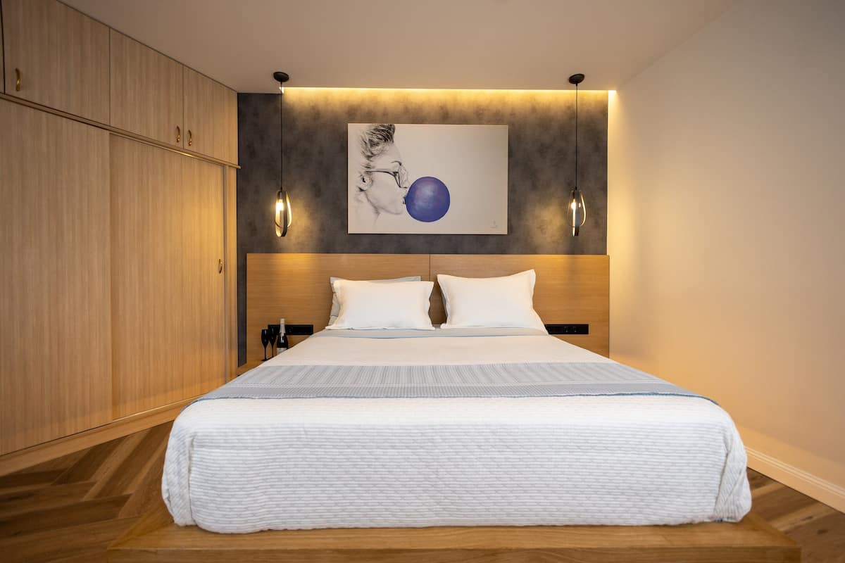 A modern bedroom with a large bed, wooden wardrobe, and a wall-mounted artwork.