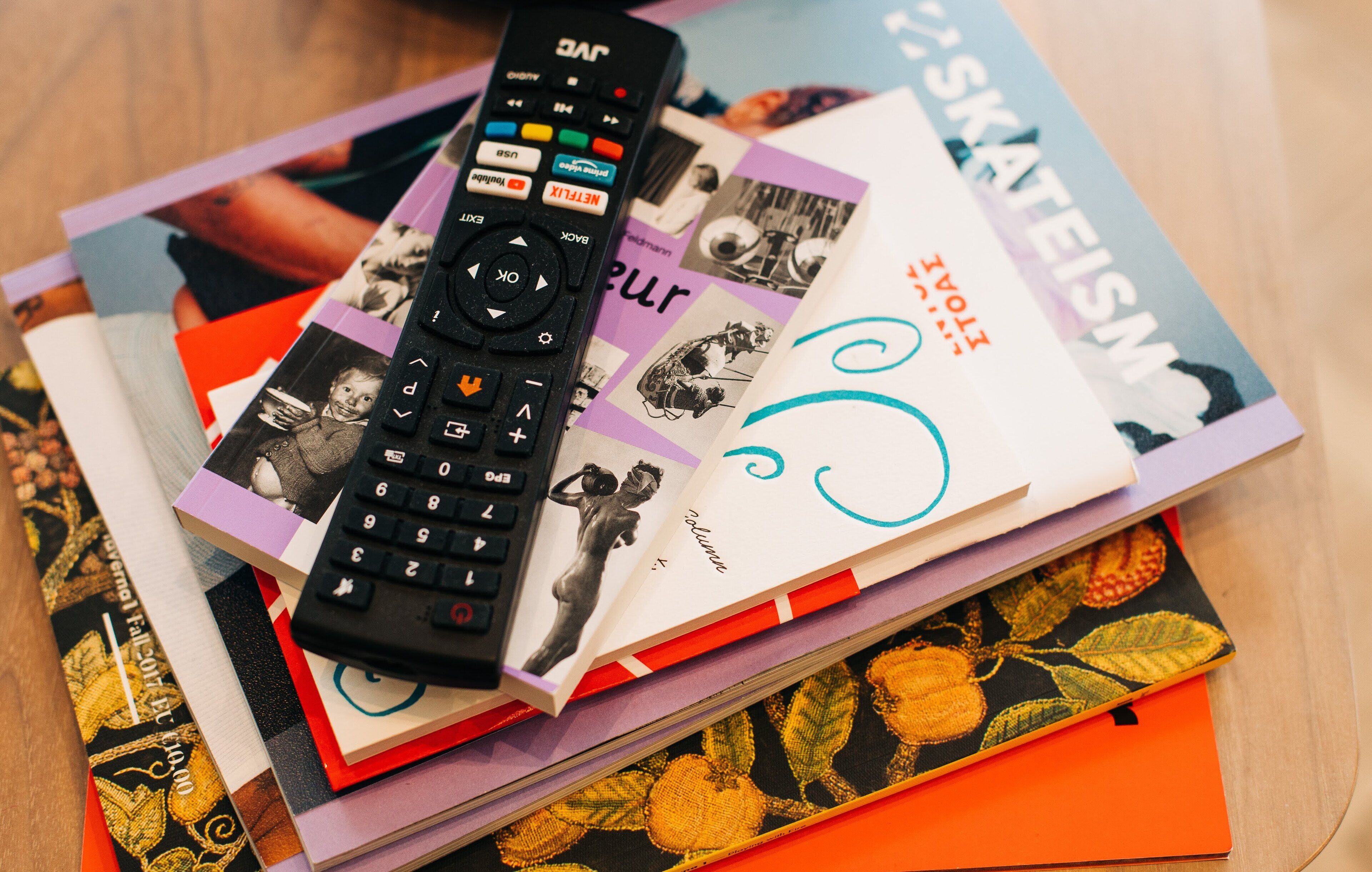 A remote control on top of a stack of magazines and books.
