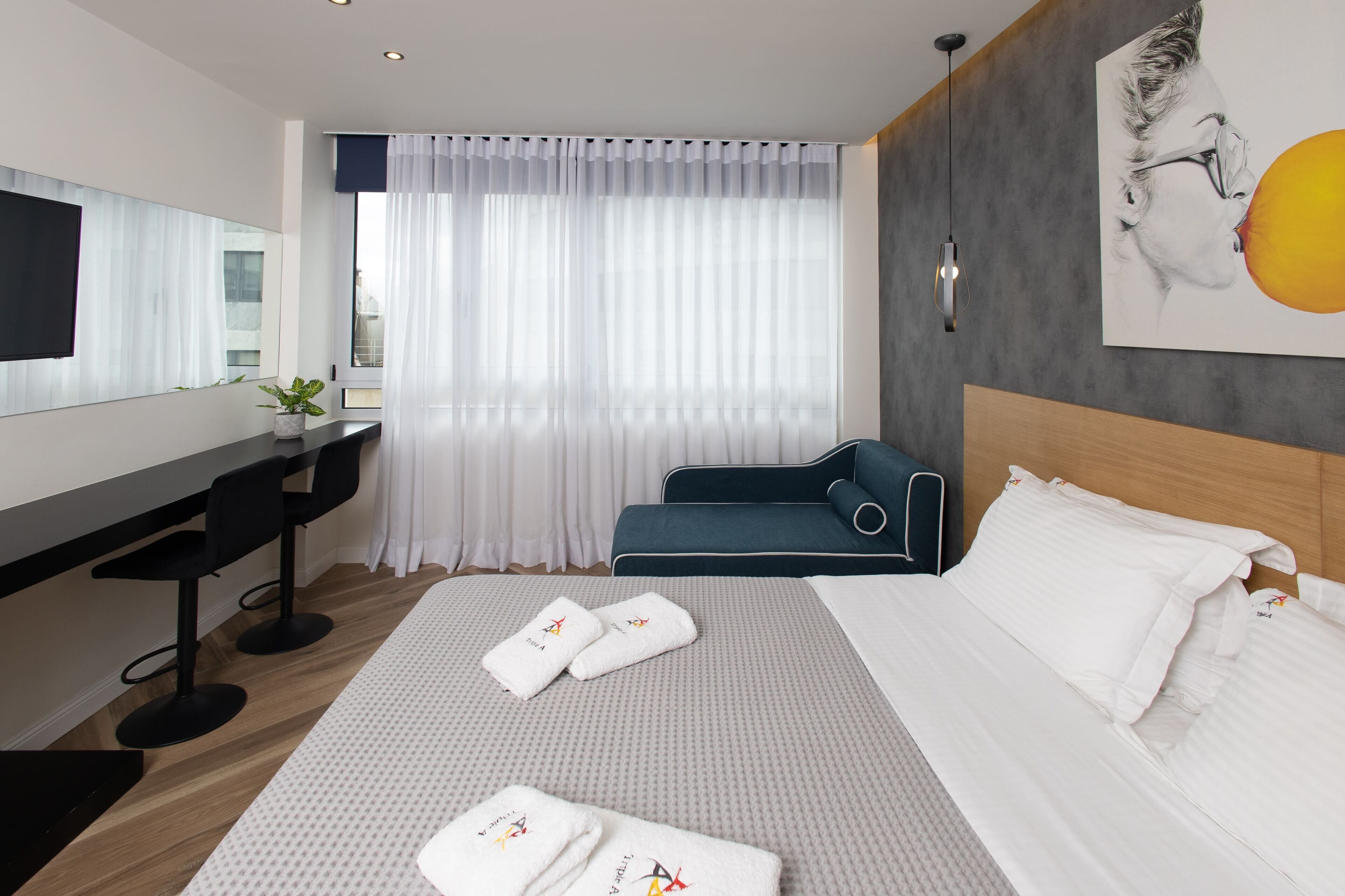 A modern hotel room with a large bed, a desk, a chair, and a sofa.