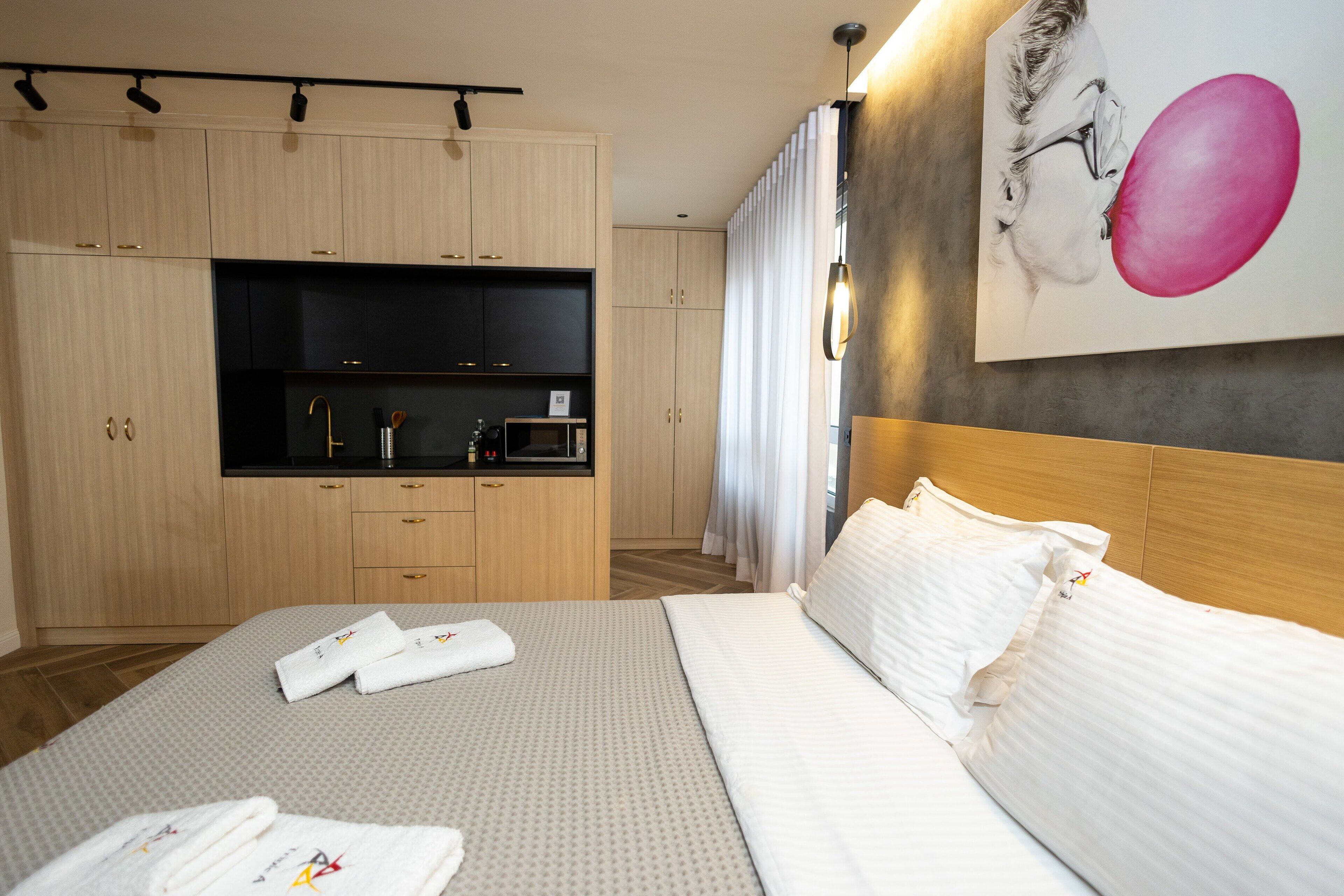 A hotel room with a bed, a small kitchenette, and a painting on the wall.