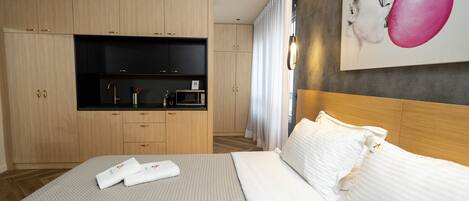 A hotel room with a bed, a small kitchenette, and a painting on the wall.