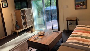 Een moderne woonkamer met een houten salontafel, een bank, een televisie en een schuifdeur naar een buitenruimte.