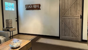 Een kamer met een schuifdeur met daarop de tekst 'Beach House', een houten tafel met een kom spullen, en een raam met uitzicht.