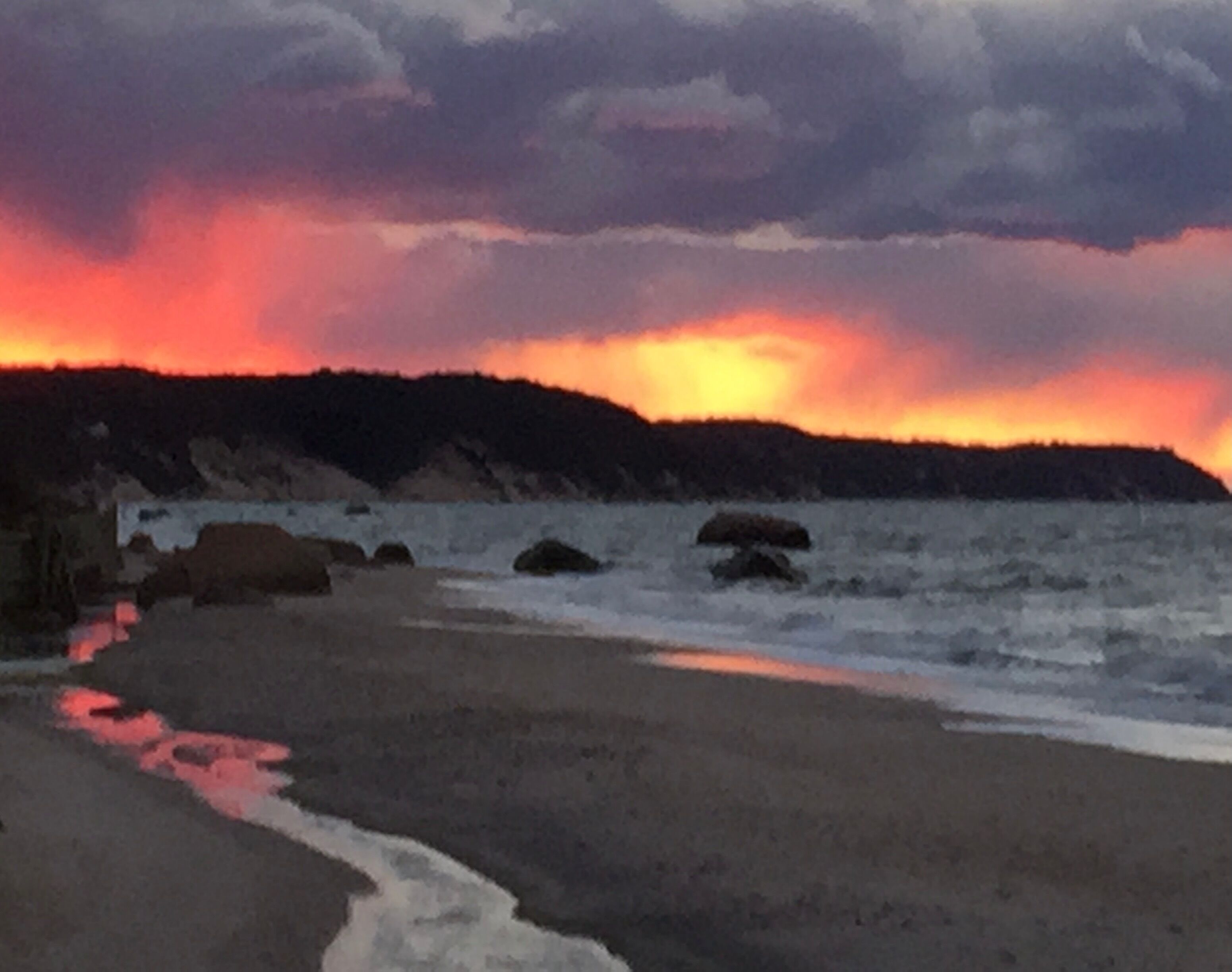 A beach with a sunset, rocky shoreline, and calm sea.