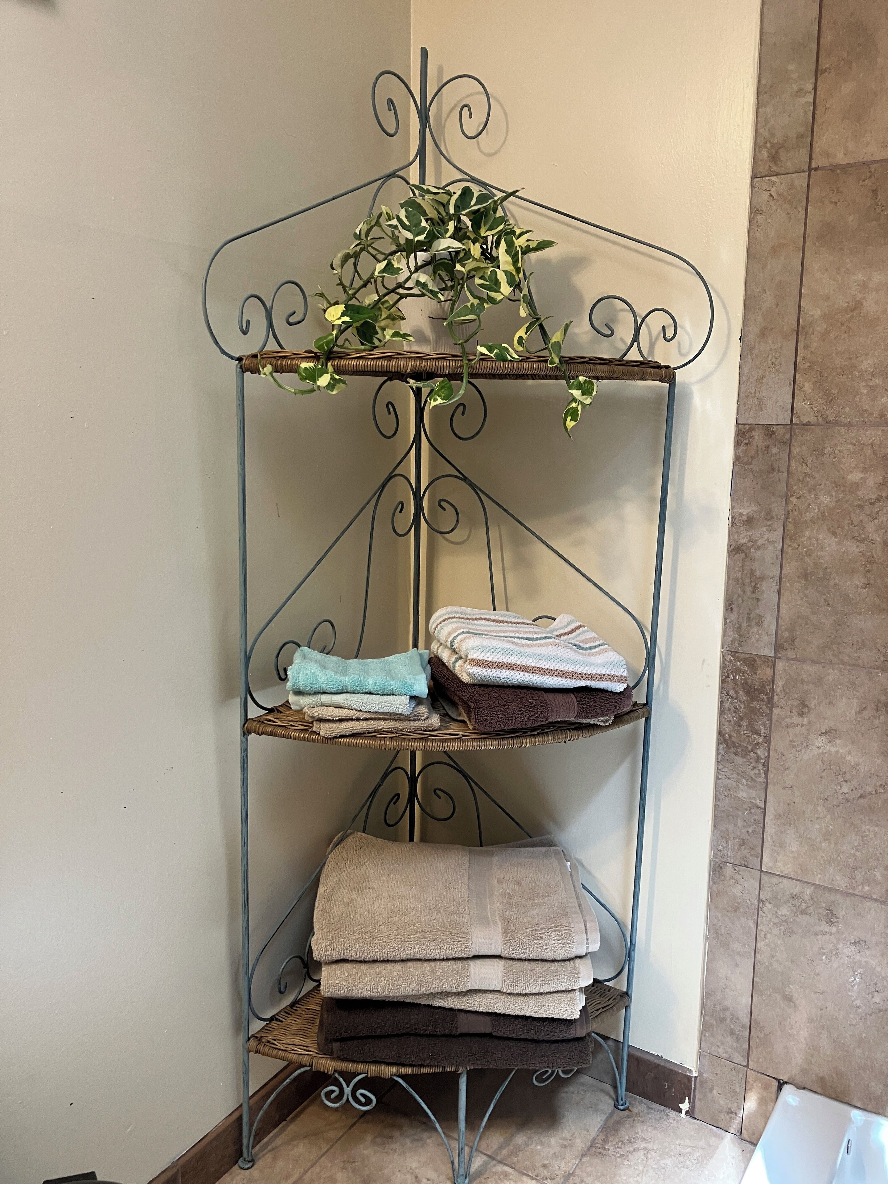 A metal shelf with three tiers holding folded towels in various colors.