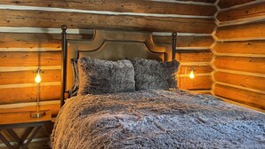 Ein gemütliches Schlafzimmer in einer Blockhütte mit einem Bett, zwei Wandlampen und einem rustikalen Holz-Kopfteil.