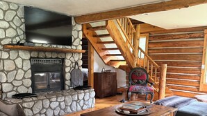 Ein gemütliches Wohnzimmer mit Kamin aus Stein, einer Holztreppe und einem bequemen Sofa.