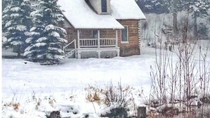 Eine Hütte mit schneebedecktem Dach, umgeben von Bäumen und einem kleinen Gewässer.
