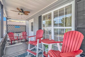 A covered porch with red Adirondack chairs and a table, a ceiling fan, and a view of the street. - Cute Cozy Beach Bungalow
golf cart available Commercial Ice maker for the cooler (Myrtle Beach)