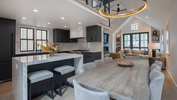 Una cocina moderna con una isla central, muebles oscuros y un amplio comedor con sillas tapizadas en gris.
