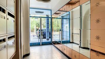 A hallway with a glass door leading outside, a tiled floor, and a wall with a decorative pattern.