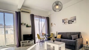 Un salon moderne doté d’un téléviseur à écran plat, d’un canapé gris, d’une table basse et d’un coin repas avec une petite table et des chaises.