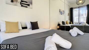 A modern hotel room with a sofa bed, a large mirror, and a view of the outdoors.