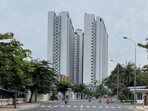 Rua com edifícios residenciais altos, árvores e faixa de pedestres.