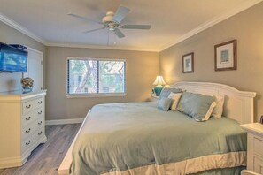 Quarto com cama, ventilador de teto, televisão, janela e cômoda.
