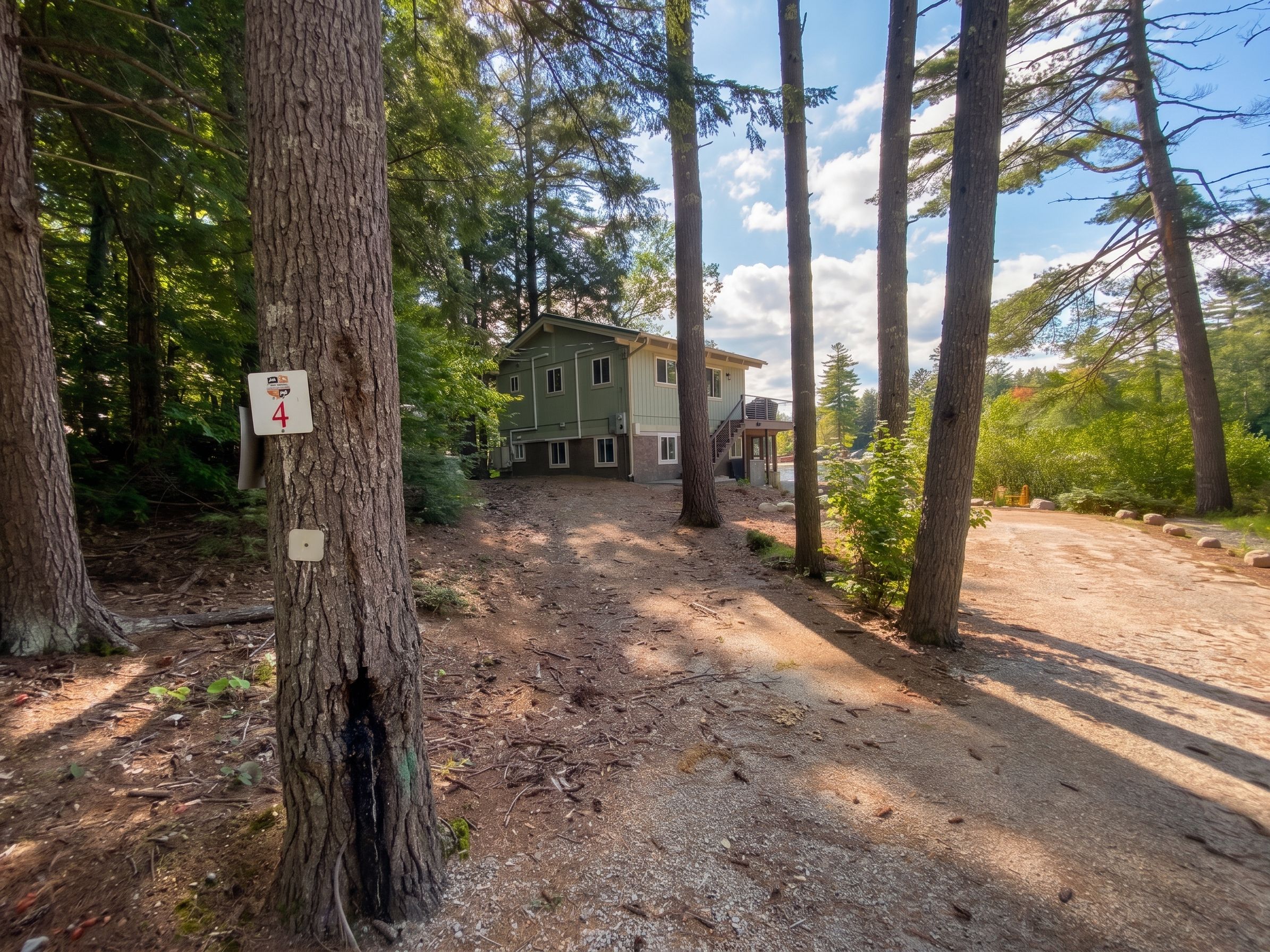 A forested area with a house, a dirt path, and a sign indicating a trail number.