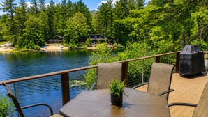 Eine Terrasse mit Tisch und Stühlen mit Blick auf einen See, umgeben von Bäumen und einer Holzhütte.