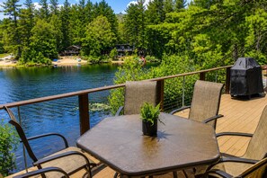 Eine Terrasse mit Tisch und Stühlen mit Blick auf einen See, umgeben von Bäumen und einer Holzhütte.