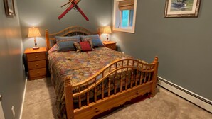 A bedroom with a wooden bed, two bedside tables, a window with a view, and a wall-mounted ski rack. - Pond-Side Chalet • Private Beach • Canoe & Kayak • Sleeps 7 • Near Storyland (Madison)