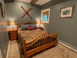 A bedroom with a wooden bed, two bedside tables, a window with a view, and a wall-mounted ski rack.