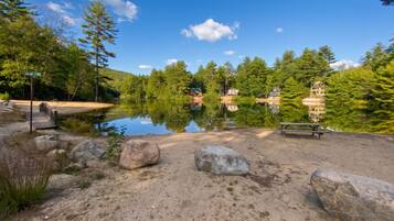 A lakeside campsite with a picnic table, large rocks, and cabins in the background.