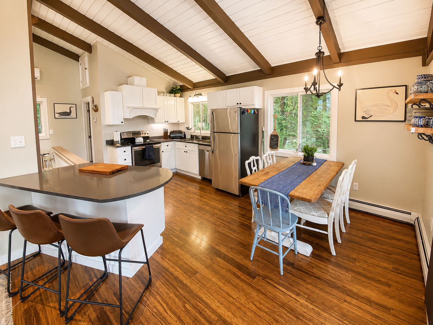 A modern kitchen with white cabinets, a central island, and a dining area with a wooden table and chairs.