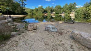 A tranquil lakeside setting with a wooden dock, a picnic table, and a clear view of a house across the water. - Pond-Side Chalet • Private Beach • Canoe & Kayak • Sleeps 7 • Near Storyland (Madison)