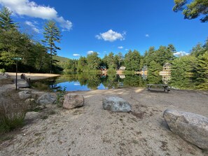 Un entorno tranquilo junto al lago con un muelle de madera, una mesa de picnic y una vista despejada de una casa al otro lado del agua.